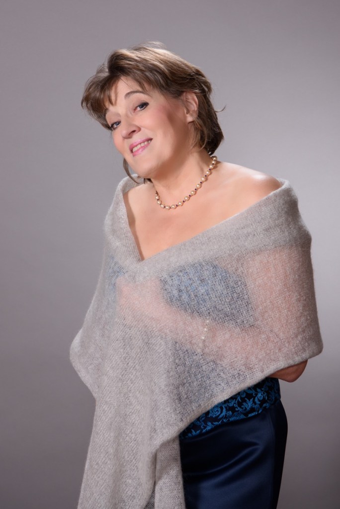 Kuvassa laulajatar Eini Annukka Perälä sinisessä laulajamekossaan ja vaalean harmaa huivi harteilla.